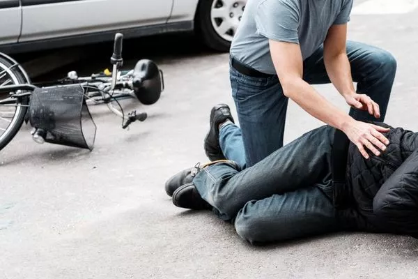 pedestrian-helping-a-victim-of-an-automobile-accident-lying-on-the-street-next-to-a-broken-bike